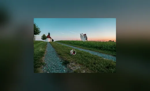 Feldweg zu einer Kapelle bei Sonnenuntergang, ein Brautpaar in der Ferne